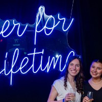 Group of three girls stand in front of Laker for a Lifetime neon sign